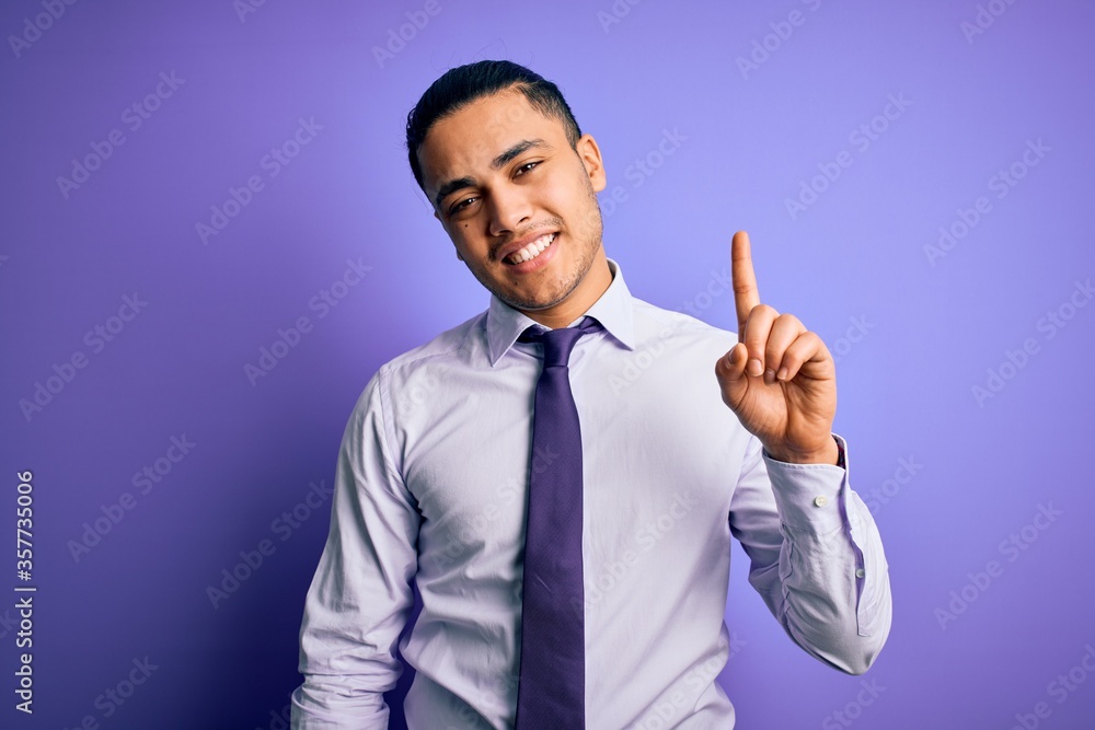 Young brazilian businessman wearing elegant tie standing over isolated purple background pointing finger up with successful idea. Exited and happy. Number one. Young brazilian businessman wearing elegant tie standing over isolated purple background pointing finger up with successful idea. Exited and happy. Number one.