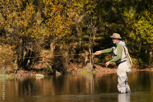 Side view of man with beard fly fishing on a river in the Fall season