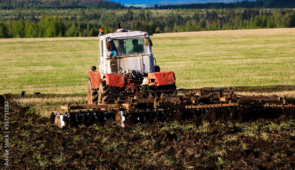  tractor plows and harrows  land in  large field on  sunny spring day. preparing  soil for planting crops, plowing  soil with  tractor with  disk plow.