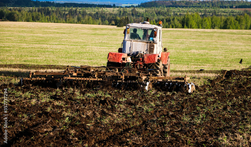 tractor plows and harrows land in large field on sunny spring day. preparing soil for planting crops, plowing soil with tractor with disk plow. tractor plows and harrows land in large field on sunny spring day. preparing soil for planting crops, plowing soil with tractor with disk plow.