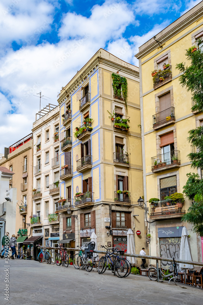 Ground floor shops, apartments with plants hanging on balconies, parked bicycles and people walking, in Barcelona, Spain
