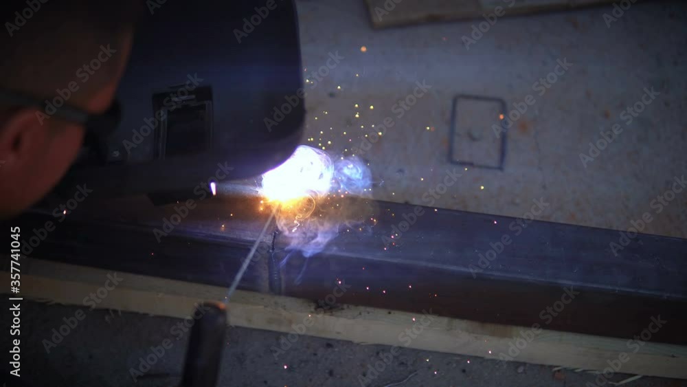 Young welder in protective mask leaning over workbench and welding iron work pieces Young welder in protective mask leaning over workbench and welding iron work pieces