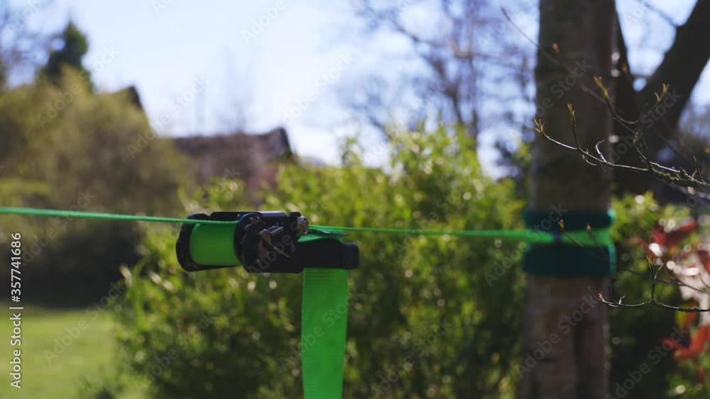 Closeup of bright green slack line and ratchet on slightly windy but very sunny day. Blue sky. Green bush and silver birch tree in background. Closeup of bright green slack line and ratchet on slightly windy but very sunny day. Blue sky. Green bush and silver birch tree in background.