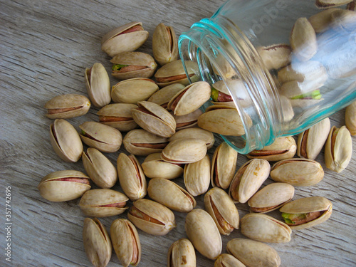 Pistachios scattered  from a glass bottle on a wooden table. Iranian In-Shell Pistachios. This is a type of Iranian commercial pistachio called Akbari Pistachio (Super Long Pistachio). Close up... photo