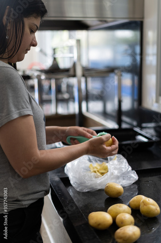 mulher de cabelos pretos, descascando batata e cozinhando a refeição para o almoço da família. 