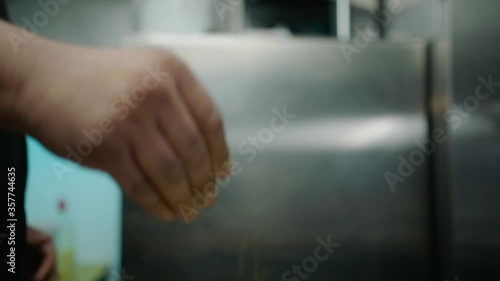 Slow motion HD 50fps shot of a chef sprinkling herbs and spcies onto raw chicken in a professional kitchen setting. The chicken is being marinated in asian herbs and spices including bay leaves.