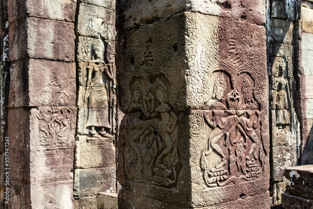 Carved column with female dancers (apsaras) in movement wearing diadems at Banteay Kdei temple. Red limestone. Angkor area, Siem Reap, Cambodia, South east Asia