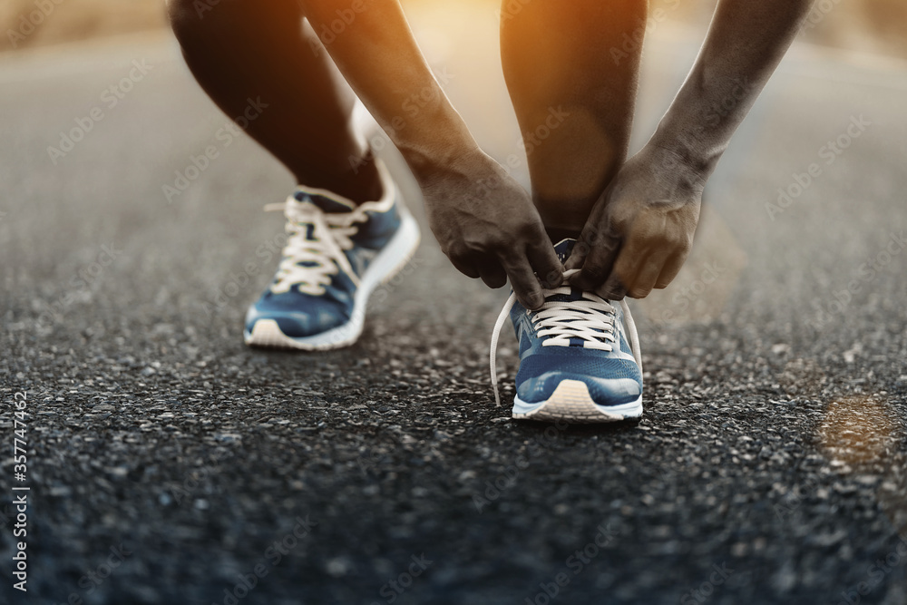 Young African American man runner tying shoelaces on road in outdoor.