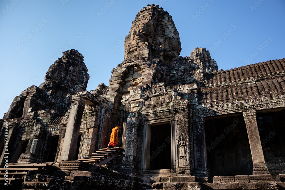 Buddhist monk dressed in orange climbing stairs entering a door at the facade of Bayon temple at the center of Angkor Thom complex in Siem Reap, Cambodia, South east Asia.