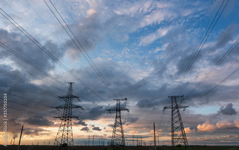 High-voltage power lines passing through a green field of wheat, on the background of a cloudy sky