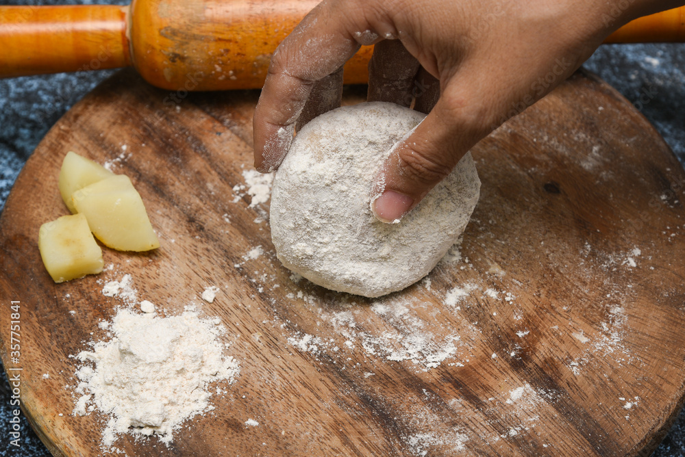 Obraz premium Preparation of Aloo Paratha or roti parantha chapati Punjab, North India. Female hand rolling whole wheat dough mashed potato stuffing with rolling pin. Indian side dish raita, dal makhani.