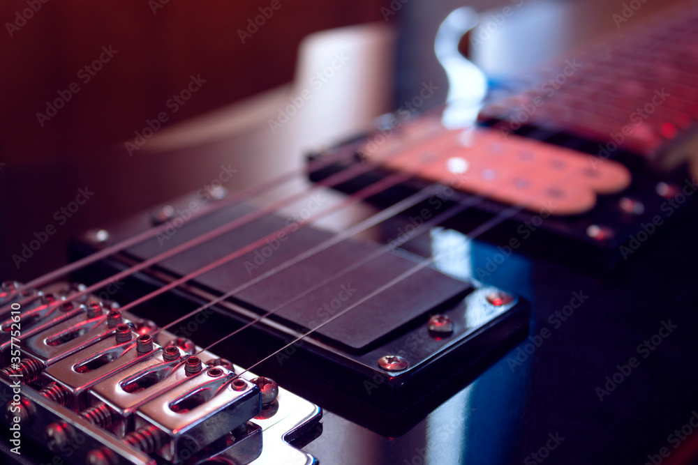 Fototapeta premium closeup to a six black electric guitar strings, wooden fretboard and microphones iluminated with red ligths. Instruments and music concept