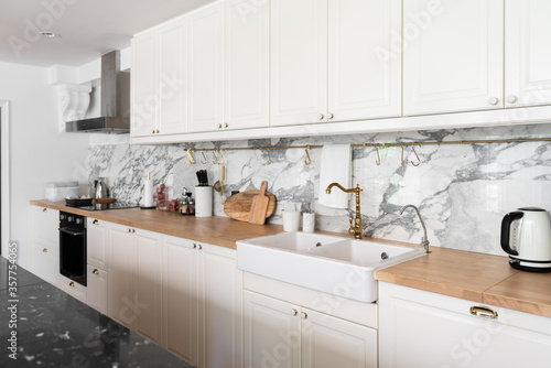Fototapeta Naklejka Na Ścianę i Meble -  Modern classic kitchen interior with kitchen appliances and white ceramic sink with gold mirror faucet on wood top with marble wall in the background / kitchen interior