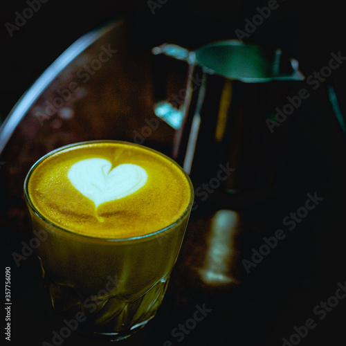 Heart latte art and milk jug on wood table.