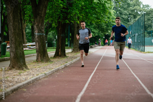  Young men training on a race track. Two young friends running on athletics track
