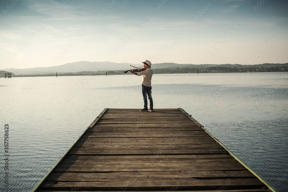 boy plays the violin on the lake