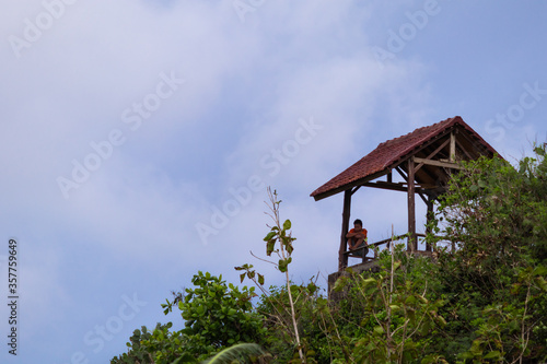 Bali, Indonesia; February 2020: Lonely young man sitting under the roof of a hut in the jungle looking at the horizon, like a bird in a cage. Editing space. Bali, Indonesia, Southeast Asia
