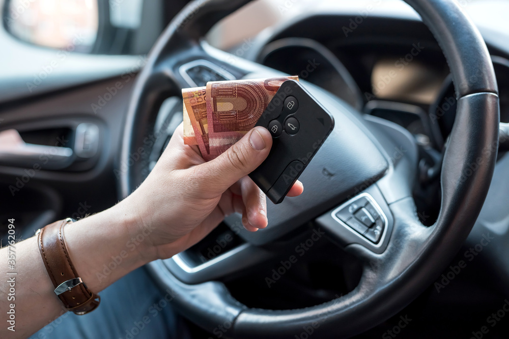 Naklejka premium male's hand holding euro bills and key inside car for buy or rent