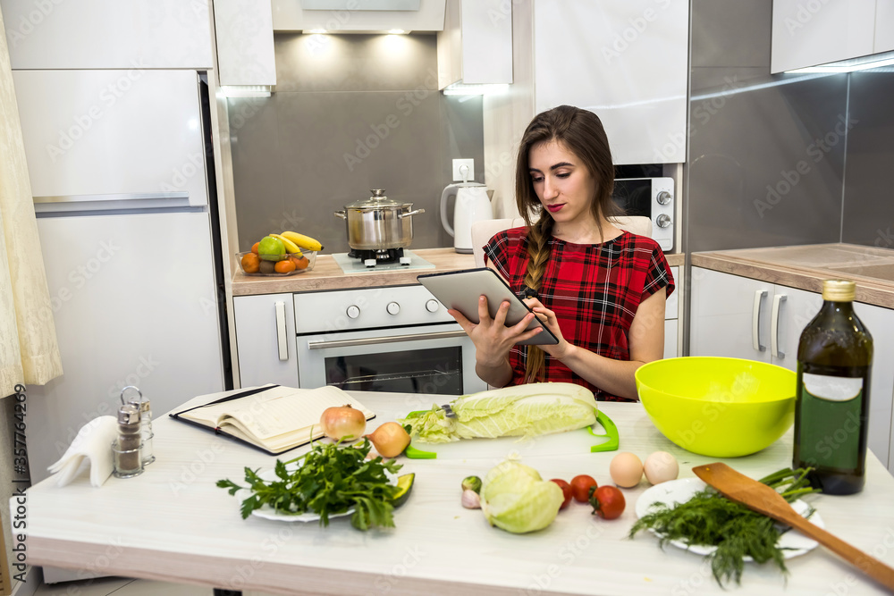 Young woman using a tablet computer to cook different vegetables in her kitchen for everything about healthy nutrition.