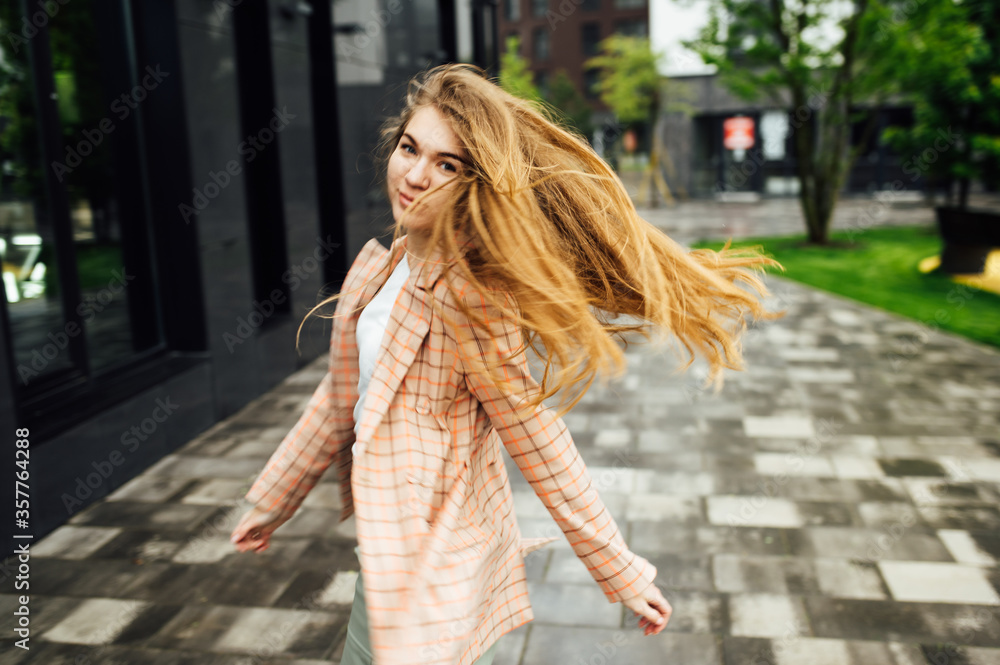 Beautiful girl walks in the city near the black wall in the rain