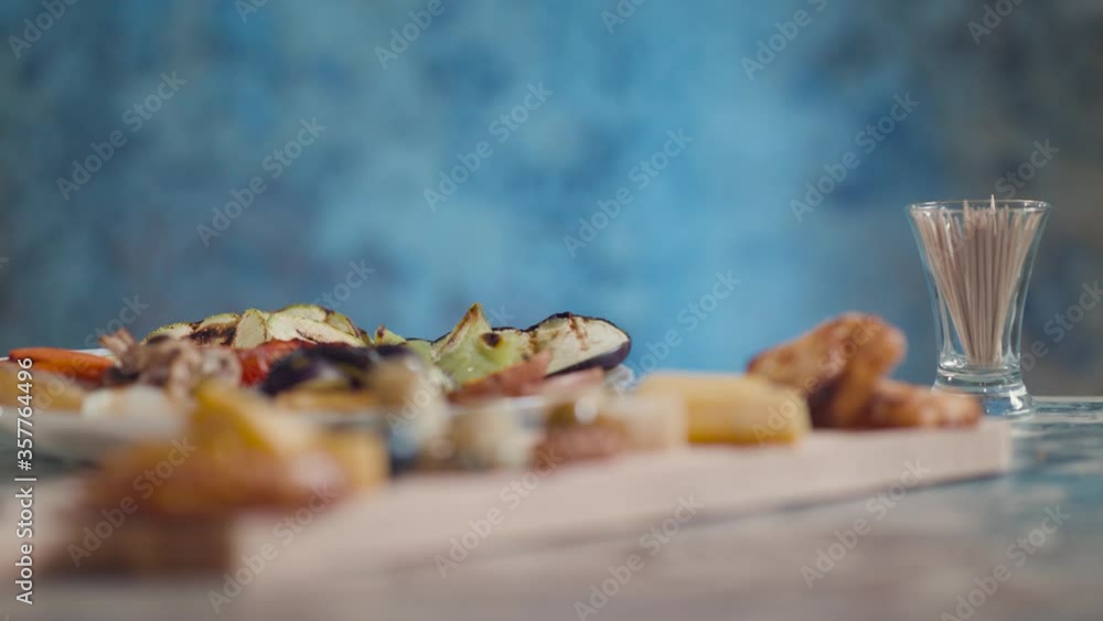Someone puts the plate next to the board with crackers cheese nuts and olives Someone puts the plate next to the board with crackers cheese nuts and olives