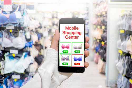 Woman hand use mobile smart phone to shopping online with blurry background of bra and lingerie in women underwear department
