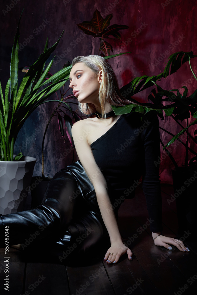 Fashion woman sitting on the floor in tropical foliage pink light. Wet hair, perfect figure and makeup. Beautiful blonde girl and monster leaves Fashion woman sitting on the floor in tropical foliage pink light. Wet hair, perfect figure and makeup. Beautiful blonde girl and monster leaves
