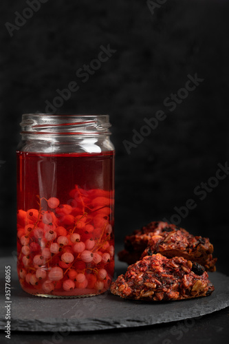 A pile of homemade oatmeal cookies tied with rope against background of red currant fruit juice jar staying on stony dark grey serving platter