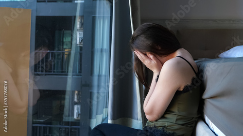 upset sleepy woman with long loose hair sits near large bed and window in comfortable hotel room in early morning © lenblr
