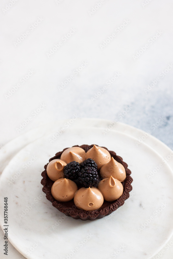 Chocolate mini tart with whipped caramel cream and fresh blackberry. Plain white background. Chocolate mini tart with whipped caramel cream and fresh blackberry. Plain white background.
