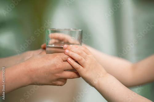 Close-up of a man's hand giving a glass of fresh filtered water to a child.