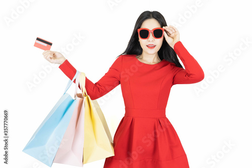 Happy Young beautiful asian woman in red dress wearing fashion sunglasses carrying color pastel shopping bag isolated on white background