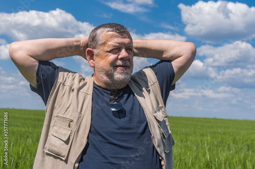 Portrait of smiling senior farmer standing inside unripe wheat field