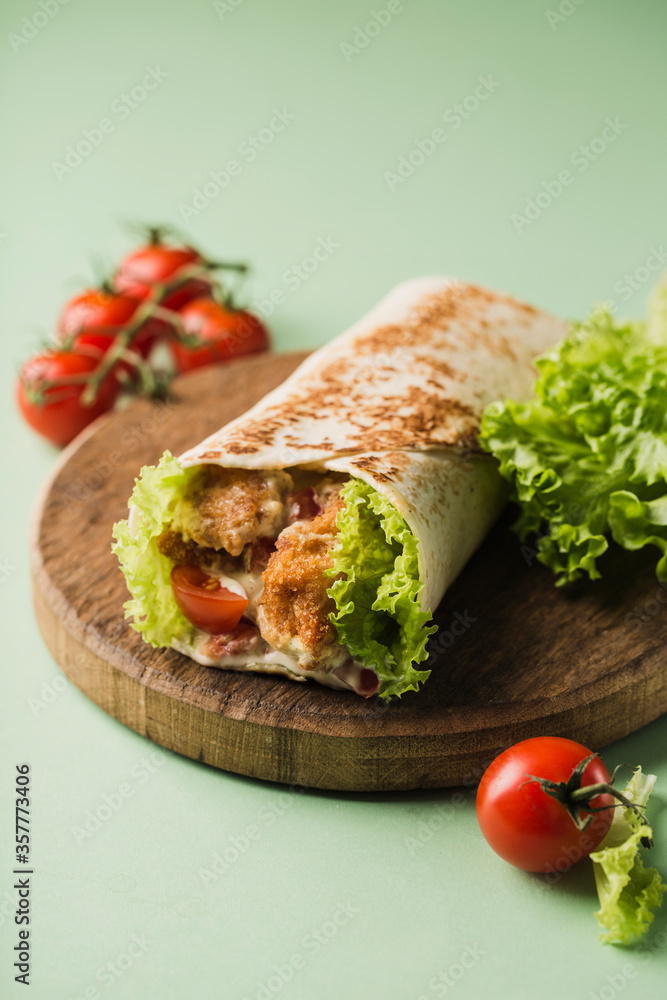 Roll with chicken and fresh cherry tomatoes and lettuce on a wooden Board on a bright green background. Roll with chicken and fresh cherry tomatoes and lettuce on a wooden Board on a bright green background.