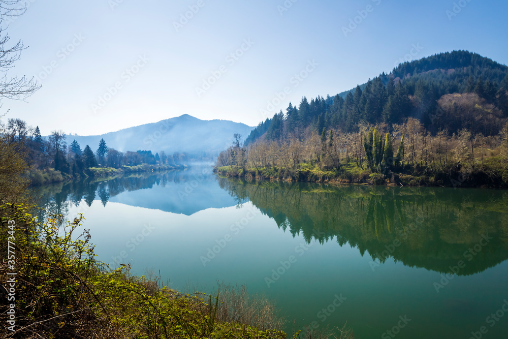 Beautiful river landscape in the early morning with reflection of hills with wooded banks in calm water. Umpqua river in Oregon