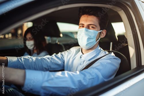 Young boy taxi driver gives passenger a ride wearing sterile medical mask. A man in the car behind the steering wheel works during coronavirus pandemic. Social distance and health safety concept. © Konstantin Zibert