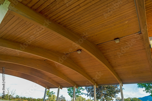 Close up of the brown wooden roof of a pavilion with arched beams and lights