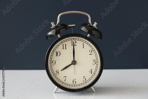 Black vintage alarm clock on white surface and isolated on dark blue background.