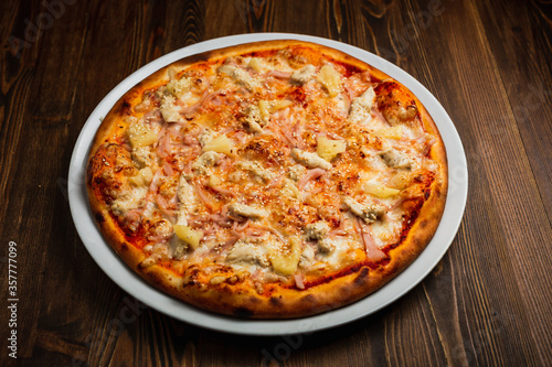Ham, cheese, chicken meat and pineapple pizza, wooden background, low key