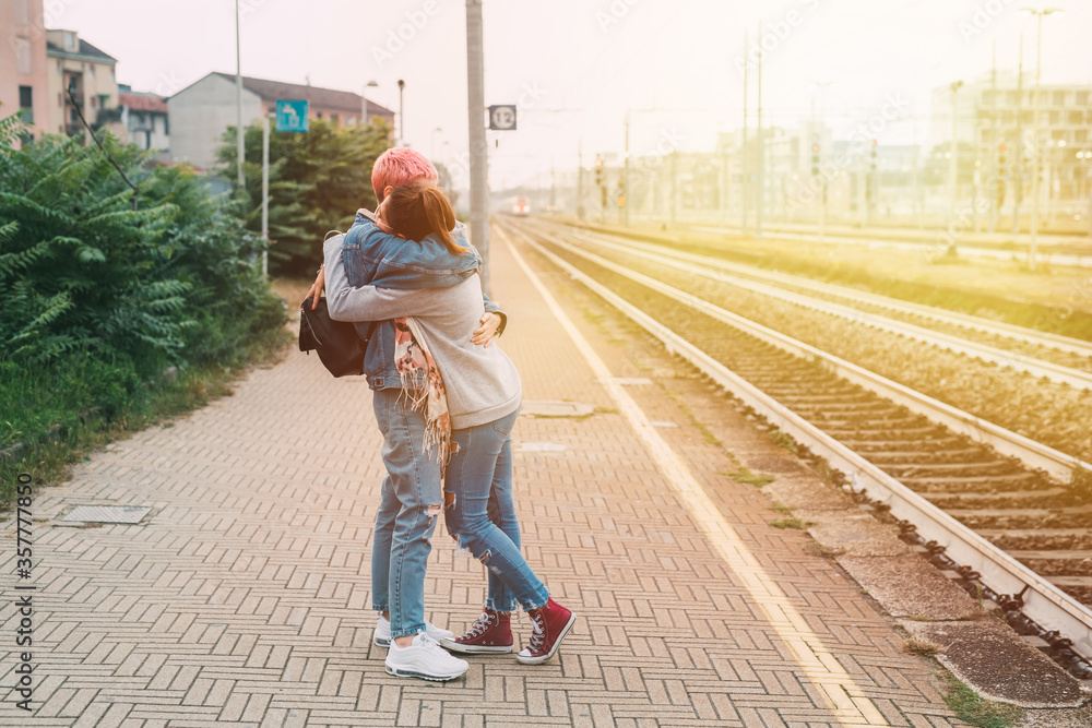 Female friends hugging railway platform saying goodbye - Two young millennials women affectionate meeting hugging train station Female friends hugging railway platform saying goodbye - Two young millennials women affectionate meeting hugging train station