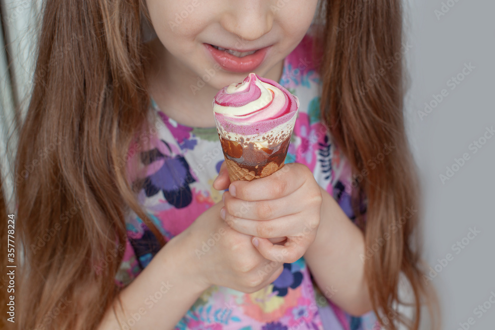 Seven year old girl eats ice cream. She holds it in her hands. Dessert with raspberry flavor. Close-up.