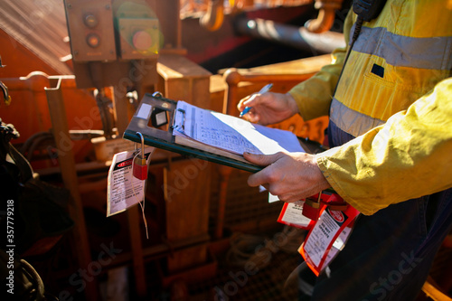 Site safety auditor supervisor verifying name of co workers on isolation lock permit board ensure are locking on and working on correct equipment prior starting each shift  