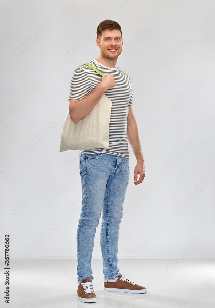 sustainability, consumerism and eco friendly concept - happy smiling man with reusable canvas bag for food shopping on grey background