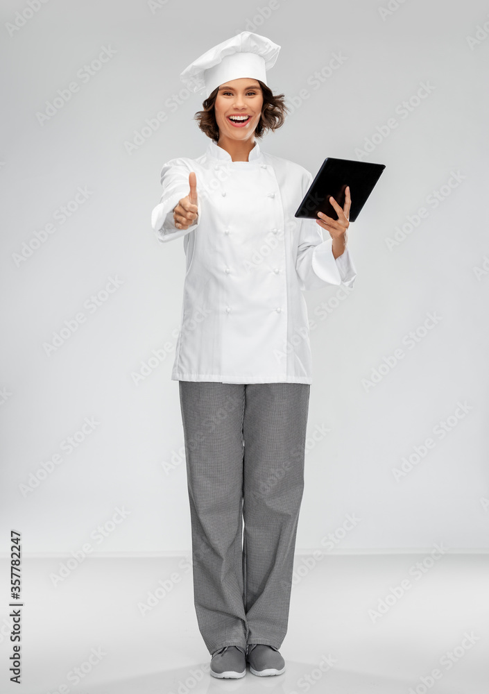 cooking, culinary and people concept - happy smiling female chef in toque with tablet pc computer showing thumbs up over grey background cooking, culinary and people concept - happy smiling female chef in toque with tablet pc computer showing thumbs up over grey background