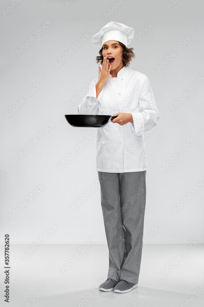 cooking, culinary and people concept - surprised female chef in toque with frying pan over grey background cooking, culinary and people concept - surprised female chef in toque with frying pan over grey background