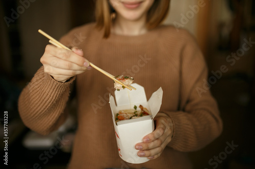 Girl in casual clothes eating noodles from a box sitting on the floor of the house  food delivery