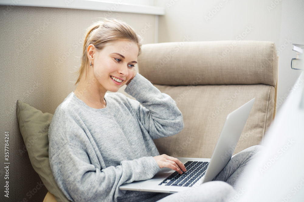 Cheerful young blonde with laptop in her hands sitting in chair on balcony Cheerful young blonde with laptop in her hands sitting in chair on balcony