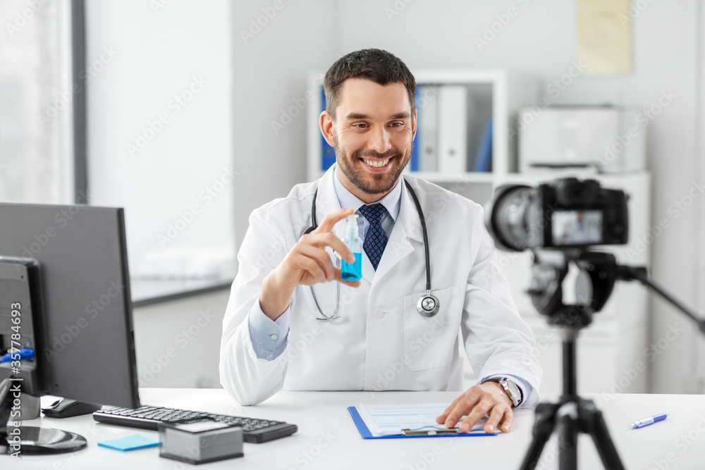 healthcare, medicine and blogging concept - happy smiling male doctor with camera and hand sanitizer recording video blog at hospital