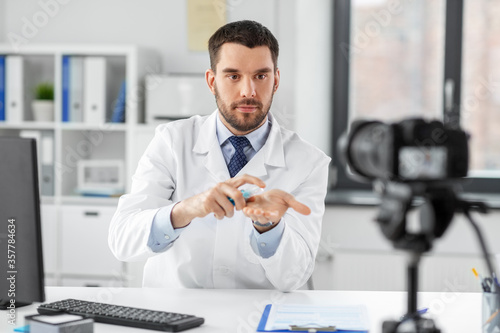 healthcare  medicine and blogging concept - male doctor with camera and hand sanitizer recording video blog at hospital