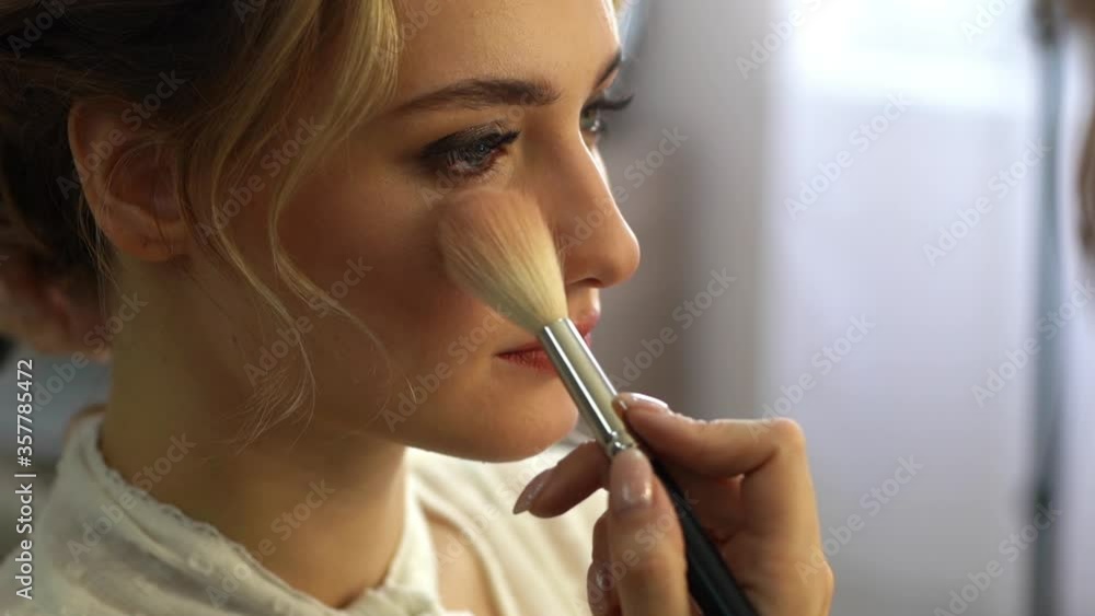 Close-up of face of young beautiful woman with long hair getting professional service in beauty salon, make-up artist putting rouge on cheek of female using brush. Shooting in slow motion. Close-up of face of young beautiful woman with long hair getting professional service in beauty salon, make-up artist putting rouge on cheek of female using brush. Shooting in slow motion.